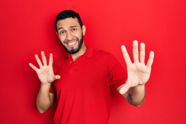 Sakallı, sıradan kırmızı tişörtlü, korku ifadesinden korkan ve dehşete düşmüş İspanyol bir adam. El kol hareketi yapmayı kes, şok içinde bağır. panik konsepti. 