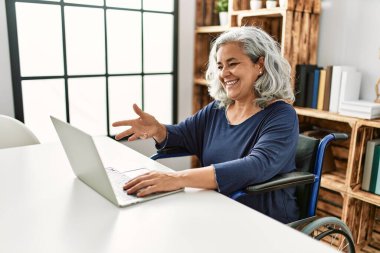 Orta yaşlı, gri saçlı, engelli bir kadın tekerlekli sandalyede otururken görüntülü konuşma yapıyor..