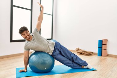 Genç İspanyol sporcu mutlu bir şekilde gülümsüyor. Spor merkezinde formda top kullanıyor..