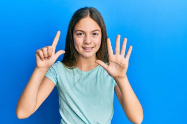 Güzel, esmer, beyaz tişört giyen küçük bir kız yedi numaralı parmaklarıyla onu gösterirken kendinden emin ve mutlu bir şekilde gülümsüyor.. 