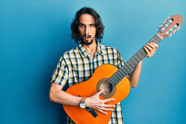 Ung Latinamerikansk Man Spelar Klassisk Gitarr Chockansikte Ser Skeptisk Och — Stockfoto