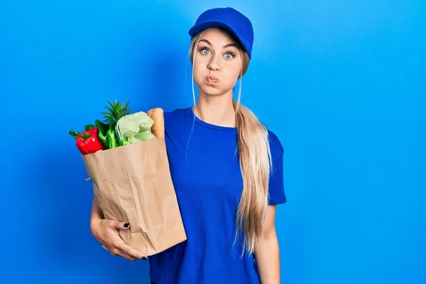 年轻的高加索女人穿着信使制服 带着杂货 从超级市场吐出一张滑稽的脸 气喘吁吁的嘴 疯狂的表情 — 图库照片