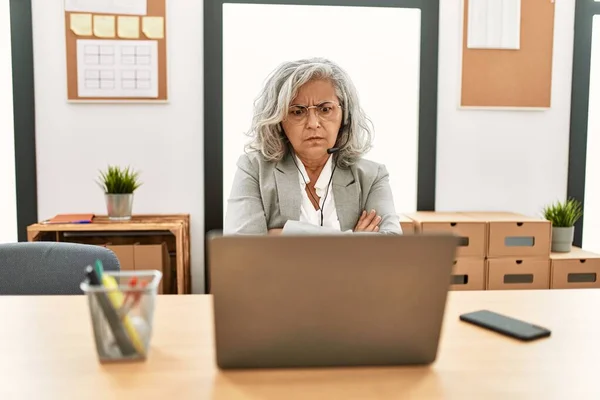 オフィスでノートパソコンを使って机の上に座っている中年の実業家は懐疑的で緊張し 両腕を組んで顔の表現を否定しています 否定的な人 — ストック写真