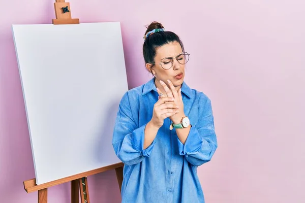 画家のそばに立つ若いヒスパニック系の女性イーゼルは手や指に痛みを我慢します 関節炎の炎症 — ストック写真
