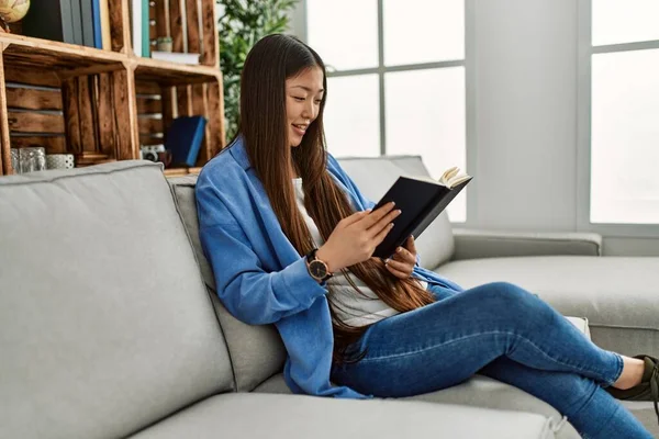 Νεαρή Κινέζα Διαβάζοντας Βιβλίο Κάθεται Στον Καναπέ Στο Σπίτι — Φωτογραφία Αρχείου