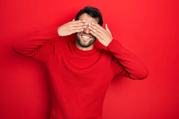 Przystojny Mężczyzna Brodą Czerwonym Swetrze Zakrywający Oczy Dłońmi Uśmiechniętymi Wesołymi — Zdjęcie stockowe