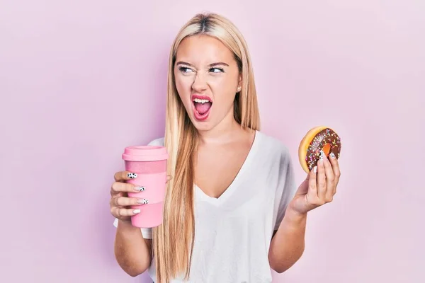 Jovem Loira Comendo Donut Bebendo Café Irritado Louco Gritando Frustrado — Fotografia de Stock