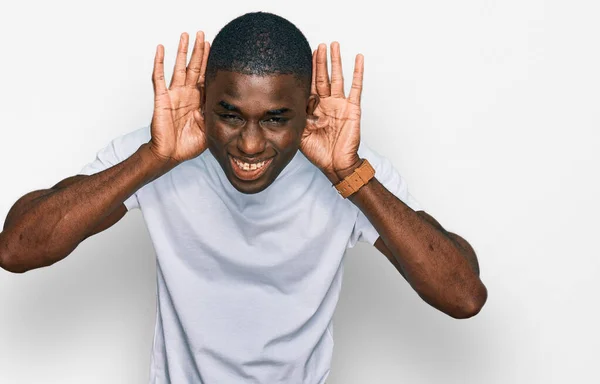 年轻的非洲裔美国人穿着宽松的白色T恤 试图用耳朵听双手的动作 好奇地听八卦 听力问题 — 图库照片