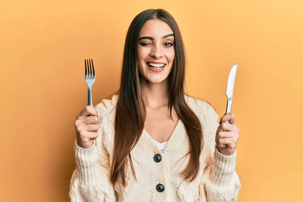 美しいブルネット若い女性がフォークとナイフを持っているセクシー表現でカメラを見てウィンクを食べる準備ができて 陽気で幸せな顔 — ストック写真