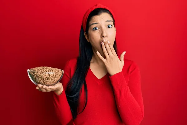 若いラテン語の女性の手で口をカバーレンズ豆とボウルを保持し ショックを受け ミスを恐れている 驚きの表情 — ストック写真