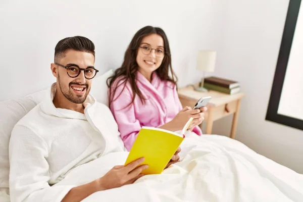 Jong Spaans Echtpaar Lezen Boek Met Behulp Van Smartphone Bed — Stockfoto