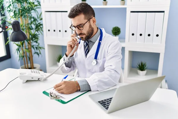 Joven Hispano Vistiendo Uniforme Médico Hablando Por Teléfono Escribiendo Portapapeles — Foto de Stock