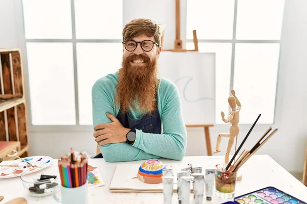 红头发的男人 留着长胡子 在艺术工作室里画着黏土碗眨眼看着镜头 脸上带着性感的表情 笑容满面 — 图库照片