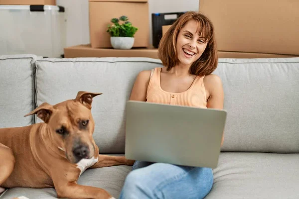 若いですCaucasian女性使用ラップトップ座っています上のソファに犬とともにホーム — ストック写真