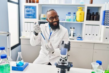 Genç Afrikalı Amerikalı adam bilim adamı üniforması giyiyor. Laboratuvarda pipetini kullanıyor.