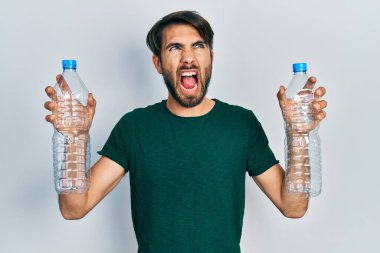 Plastik şişeleri geri dönüşüm için tutan genç İspanyol adam kızgın ve öfkeli çığlıklar atıyor, öfkeyle bağırıyor. öfke ve agresif konsept. 