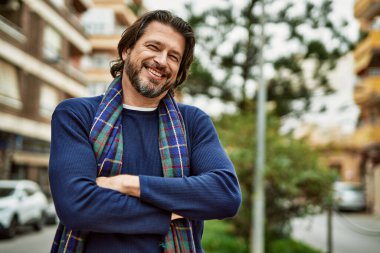 Kasabada kollarını kavuşturup gülümseyen orta yaşlı yakışıklı bir adam.