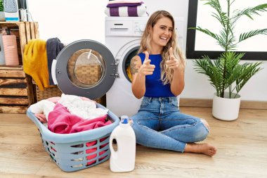 Çamaşır sepetinin yanında oturmuş, mutlu ve komik yüzüyle kamerayı işaret eden genç ve güzel bir kadın. iyi enerji ve titreşimler. 