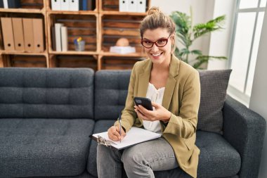 Psikoloji merkezindeki koltukta oturan akıllı telefon kullanan genç sarışın kadın psikolog.