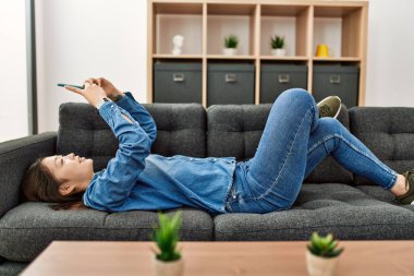 Genç Çinli kız akıllı telefon kullanıyor. Evdeki kanepede yatıyor..