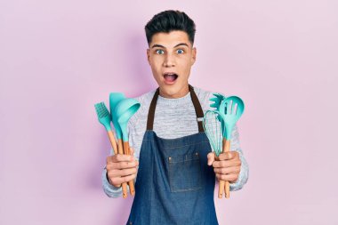 Profesyonel fırıncı önlüğü giyen genç İspanyol adam elinde yemek aletleri tutuyordu. Şaşırmış ve şaşırmış bir ifade, korku ve heyecanlı bir yüz ifadesi vardı.. 