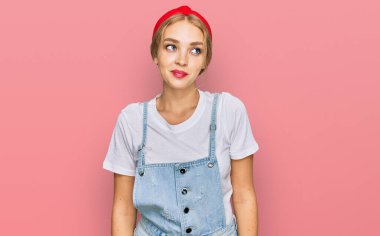 Gündelik giysiler giymiş genç beyaz kız gülümseyip yan tarafa bakıyor ve düşünüyor.. 