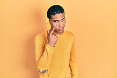 Genç Afro-Amerikalı adam müzik dinliyor. Kulaklıkla gözüne işaret ediyor. Jestini izliyor. 