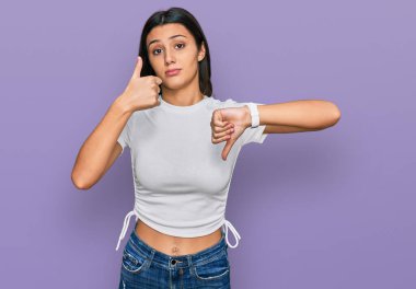 Latin kökenli genç bir kız, günlük beyaz tişört giyip baş parmak kaldırıyor, anlaşmazlık ve anlaşma ifadesi takınıyor. çılgın çatışma 