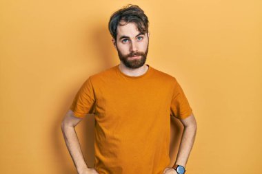 Sakallı, sıradan sarı tişörtlü, kuşkucu ve gergin bir beyaz adam, sorun yüzünden üzgün. negatif kişi. 
