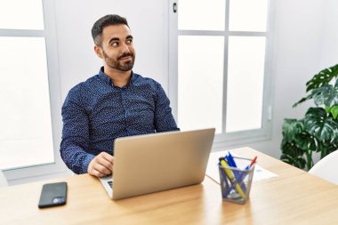 Ofiste sakallı, laptopuyla çalışan, gülümseyen ve kafasını çeviren genç İspanyol bir adam.. 