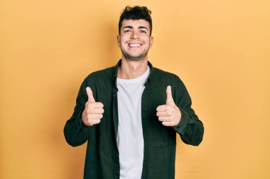 Gündelik kıyafetler giyen genç İspanyol adam. Başarı işareti yapıyor. Elleriyle olumlu jest yapıyor. Neşeli ifade ve kazanan jest. 