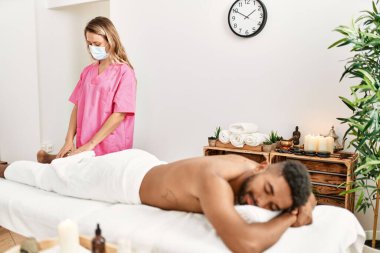 Masör kadın güzellik merkezindeki Afrikalı Amerikalı adama bacak masajı yapıyor..