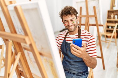 Genç İspanyol adam resim stüdyosunda akıllı telefon çizimi yapıyor.