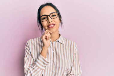 Gündelik giysiler ve gözlük takan genç İspanyol kız kameraya kollarını kavuşturup çenesini kapatarak gülümsüyor. Olumlu düşünmek. 