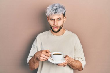 Modern boyalı saçlı genç İspanyol bir adam bir fincan kahve içiyor şüpheci ve gergin, sorun yüzünden surat asıyor. negatif kişi. 