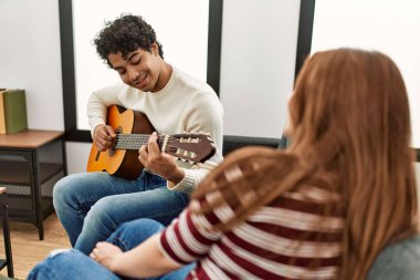 Mutlu gülümseyen genç çift evdeki kanepede oturup klasik gitar çalıyor..