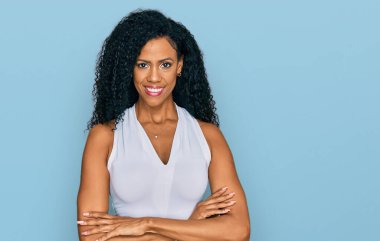 Orta yaşlı Afro-Amerikalı kadın kolsuz tişörtsüz, mutlu yüzlü, kollarını kavuşturup kameraya bakan gündelik tarzda giyiniyor. pozitif kişi. 