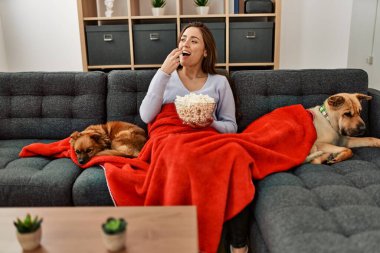 Genç İspanyol kadın evde köpeklerle kanepede oturup film izliyor.