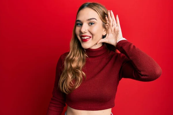 噂やゴシップに耳を傾ける耳の上に手で笑みを浮かべてタートルネックセーターを着て若いブロンドの女性 聴覚障害の概念 — ストック写真