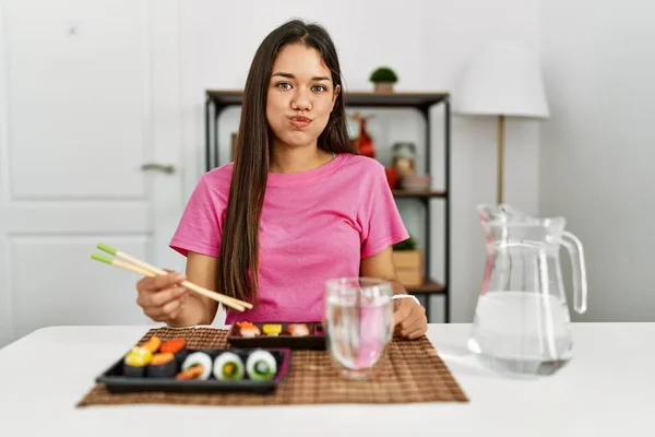年轻的黑发女人用筷子吃寿司 用滑稽的脸蛋吹着双颊 气喘吁吁的嘴 疯狂的表情 — 图库照片
