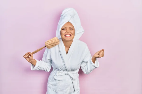 Hombre hispano vestido con maquillaje con gorro de toalla de ducha y  albornoz con una sonrisa feliz y fresca en la cara persona afortunada