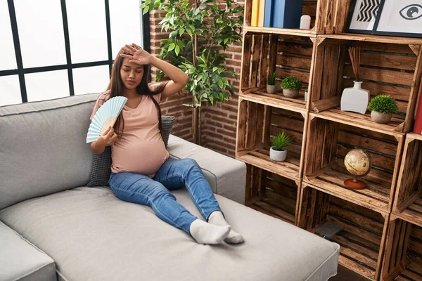Mladý Latina Žena Těhotná Pomocí Ruční Ventilátor Sedí Pohovce Doma — Stock fotografie