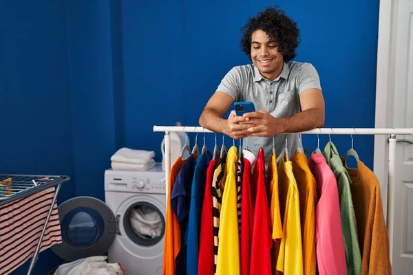 在洗衣房用智能手机靠在架子上的年轻人 — 图库照片