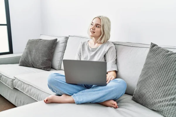 若い白人女性の自宅のソファの顔に笑顔で横に見える上に座っノートパソコンを使用して 自然な表現 自信を持って — ストック写真