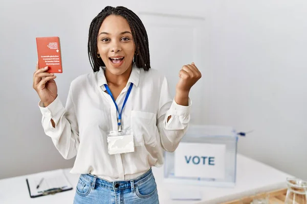 Young african american woman at political campaign election holding swiss passport screaming proud, celebrating victory and success very excited with raised arms