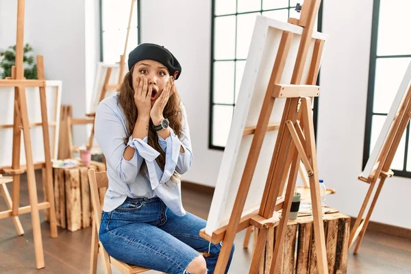 若いヒスパニック系のアーティストの女性は アートスタジオでカンバスに絵を描く顔に手で恐怖とショックを受け 驚きと驚きの表現 — ストック写真