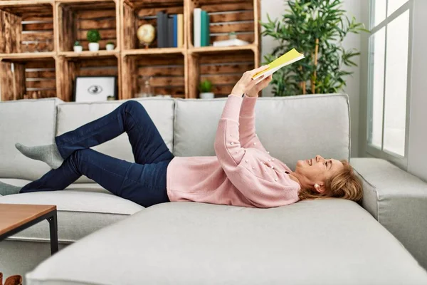 Mulher Loira Meia Idade Sorrindo Livro Leitura Feliz Deitado Sofá — Fotografia de Stock