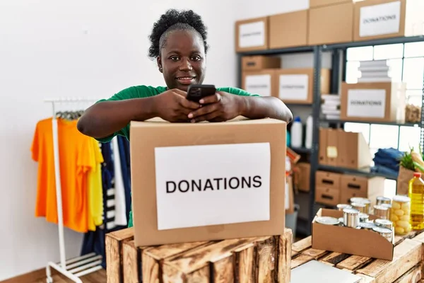 在慈善中心使用智能手机身着志愿制服的年轻非洲裔美国妇女 — 图库照片