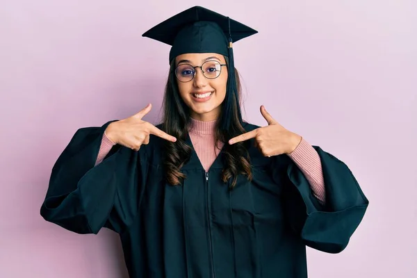 卒業キャップと式のローブを身に着けている若いヒスパニック系の女性は 誇りと幸せ指で自分自身を指して 顔に笑顔で自信を持って見えます — ストック写真