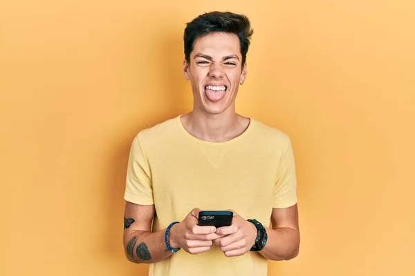 Νεαρός Ισπανόφωνος Χρησιμοποιώντας Μήνυμα Δακτυλογράφησης Smartphone Βγάζοντας Γλώσσα Χαρούμενος Αστεία — Φωτογραφία Αρχείου